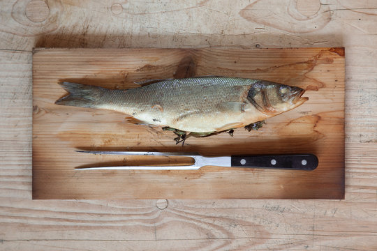 Fresh grilled sea bass, whole fish, with herbs like dill and laurel, rustic food photography on wood background