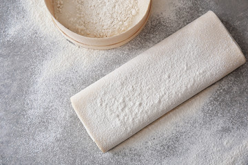 Raw flaky dough with flour on table