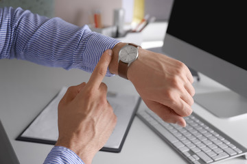 Naklejka premium Young man checking time on his wristwatch at workplace