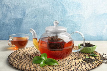 Teapot with hot aromatic tea, dry and fresh leaves on wicker mat
