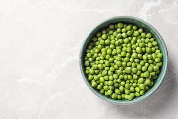 Bowl with green peas on light background, top view