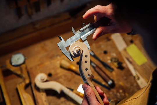 Master artisan luthier working on creation of a violin scroll. detailed work on wood with tools.