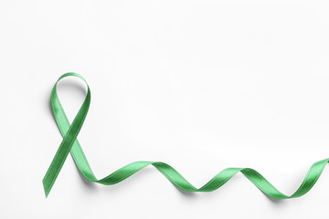 Green ribbon on white background, top view. Cancer awareness