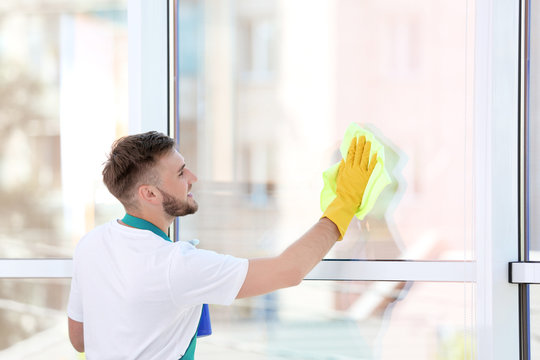 Young man cleaning window with rag indoors
