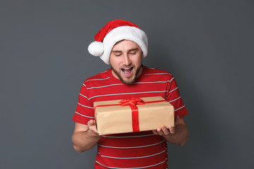 Young man with Christmas gift on grey background