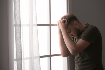 Depressed young man near window at home