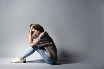 Lonely depressed woman sitting on grey background