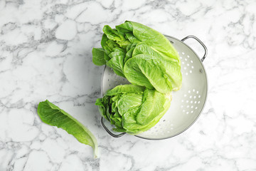 Obraz premium Colander with fresh ripe cos lettuce on marble table, top view
