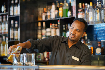 Professional bartender man holding in hands a shaker with a fresh delicious cocktail. Bartender shaking a cocktail shaker as she stands behind the bar mixing a drink for a client. Close-up.