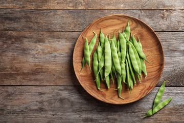 Plate with fresh green beans on wooden table, top view