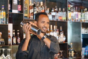 Professional bartender man holding in hands a shaker with a fresh delicious cocktail. Bartender shaking a cocktail shaker as she stands behind the bar mixing a drink for a client. Close-up.