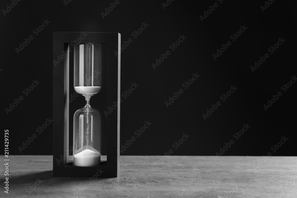 Wall mural Hourglass with flowing sand on table against black background. Time management