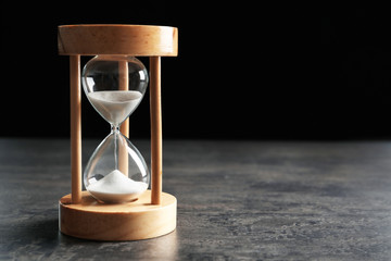 Hourglass with flowing sand on table against black background. Time management