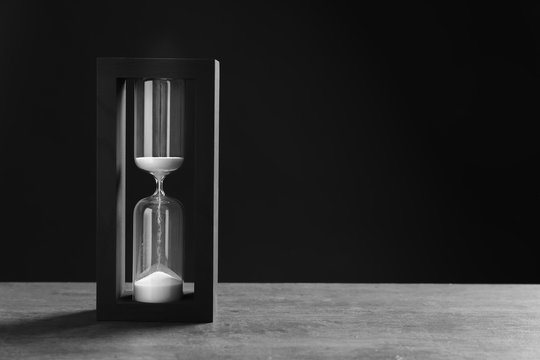 Hourglass with flowing sand on table against black background. Time management