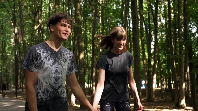 Young couple skating with roller blades in the park while holding hands in slow motion