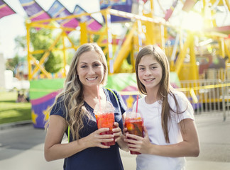 Two happy girls drinking a sweet beverage at an amusement park or summer carnival. Enjoying a cool drink on a warm summer evening