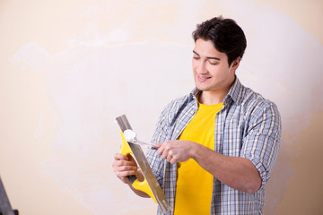 Young man applying plaster on wall at home