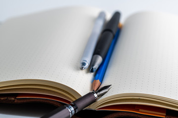 An open blank paper notebook with pen pencil and fountain pen
