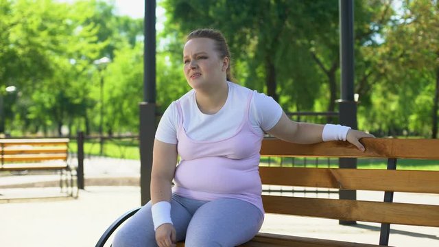 Obese woman exhausted after strenuous workouts outdoors, minute rest on bench