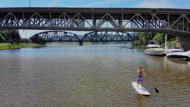 An aerial wide view of a man on a stand up paddle board on a Pennsylvania river in the summer. Pittsburgh suburbs.  	
