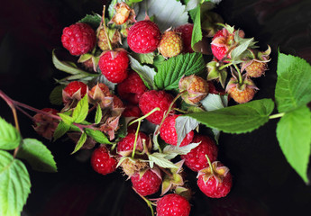 Background of berries and leaves. Raspberry (Latin Rúbus idáeus) on a black plate, top view, flat lay. Can be used for wallpapers and packaging.