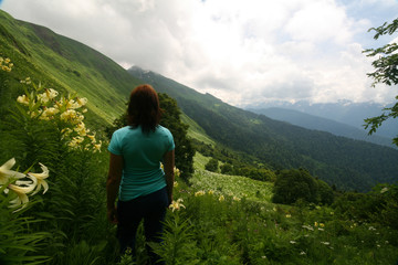 Naklejka premium Young woman among the flowering meadows in the Caucasus mountains