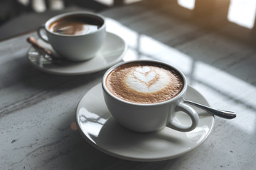Closeup image of two white cups of hot coffee on table in cafe