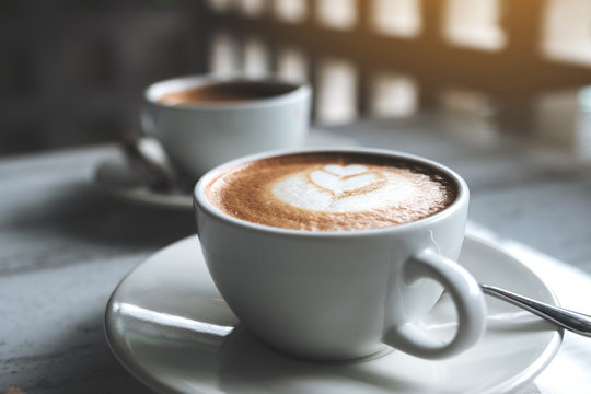 Closeup image of two white cups of hot coffee on table in cafe