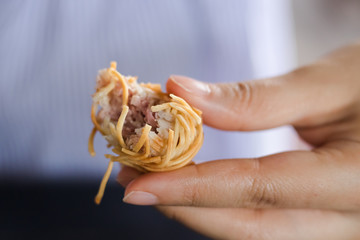 Left hand of woman holding moo sarong (Thai appetizer)