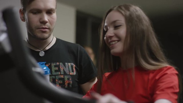 beautiful girl hardly working on exercise bike and guy come to offer her his help in the new gym