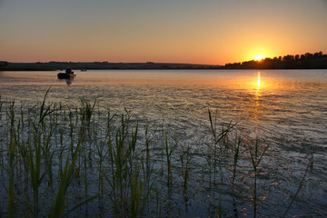 Altai Krai. Russia. An elderly fisherman on a rubber boat fishing in the summer hot evening