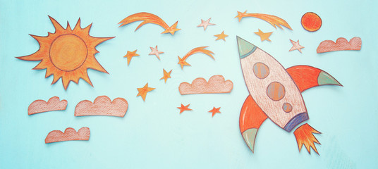 Rocket cut from paper and painted over wooden blue background.
