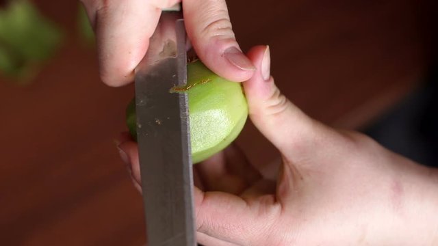 A woman cleans the kiwi peel with a knife on a wooden background. Close-up of female hands clears a kiwi, cut off the peel of the fruit, health food. Slow motion.