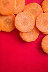 copy space with round slices of fresh orange carrot on the edges of a bright red background