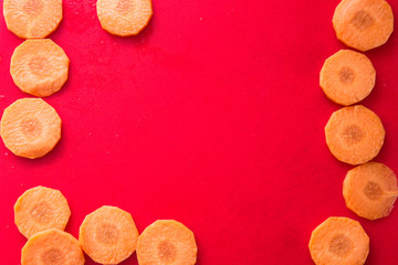 copy space with round slices of fresh orange carrot on the edges of a bright red background