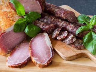 Dry sausage and meat are rustic on a wooden board and a gray background with garlic and basil.