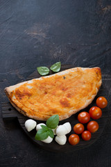 Italian calzone pizza over dark brown stone background, vertical shot with copyspace, high angle view
