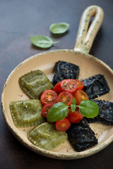 Black and spinach ravioli with cherry tomatoes and fresh green basil in a serving pan, vertical shot