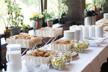 white dishes with bakery on the table with flowers on a window sill on the background