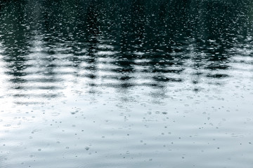 raindrops rippling on lake with trees reflecting in water during bad wether