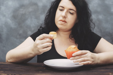 Overweight woman choosing between little and big muffins. Sense of proportion, cheat meal, portion...