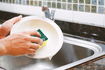 Hands in rubber gloves washing dishes with spon