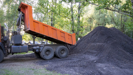 The dump truck unloads asphalt on the ground. Pile of crushed asphalt