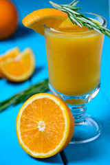 Orange fresh juice, orange pieces and green herbs on blue table