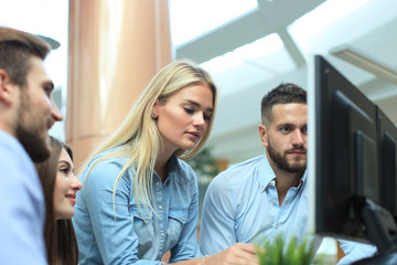 Group of young modern people in smart casual wear having a brainstorm meeting while standing in the creative office.