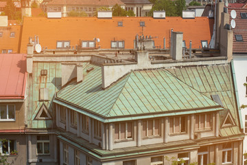 The roofs of Prague are made of red tiles and green material and are illuminated by the sun. View from the drone on the city landscape. Many Windows in the roofs of buildings.