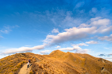 A hiker hiking on the beautiful track with a landscape of the mountains and Lake Wanaka. Roys Peak Track, South Island, New Zealand.