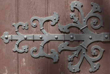 Forged metal hinge for gates and doors in the old style. Sharp curls of the iron door canopy are handmade by the blacksmith. Metal detail on the wooden surface.