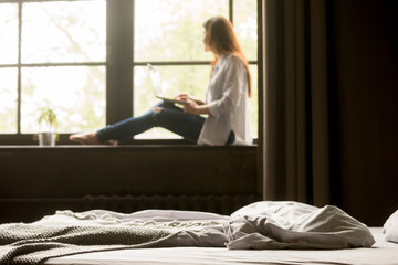 Thoughtful young woman dreaming looking in window working at laptop sitting on bedroom windowsill...
