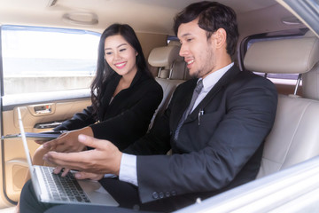 handsome businessman and Business woman sitting in luxury limousine car, working on laptop computer, Works anytime and anywhere concept.